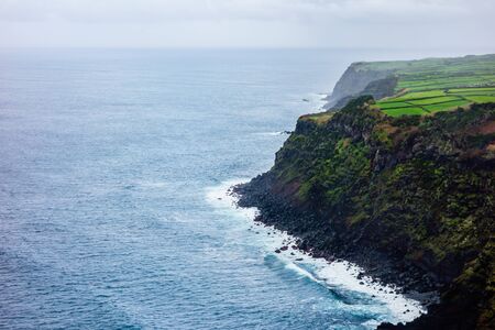 Ocean at high cliffs with lush farms on plateau, in Azores, Portugal.の写真素材