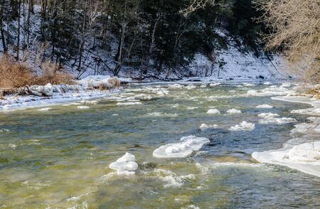 River flowing in winter with chunks of ice and snow.