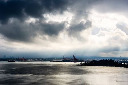 Sun breaking through from behind dark clouds in high contrast over water in Vancouver, British...
