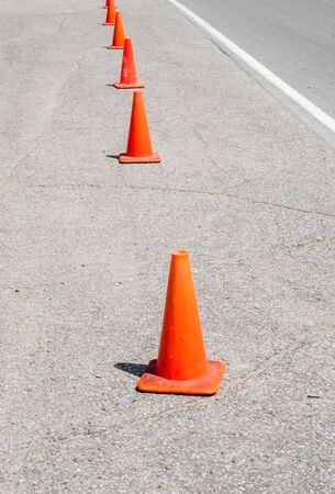Row of orange traffic cones in perspective parallel to white line on asphalt.の写真素材