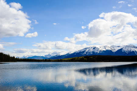 Small lake before mountains under clouds and sky, in Jasper, Alberta, Canada.の写真素材