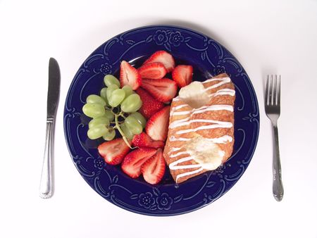 Pastry, grapes and strawberry on a blue plate with utensilの写真素材