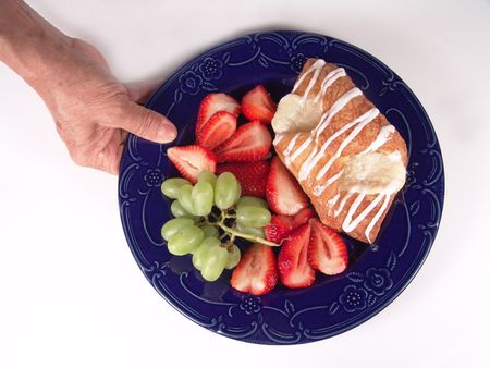Pastry, grapes and strawberry on a blue plate holding by handの写真素材