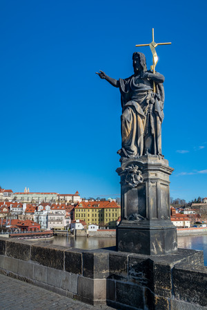Prague, Czech Republic - April 5, 2018 : Detail of a statue on the Charles Bridge and the old tower by the river, with tourists visiting.のeditorial素材