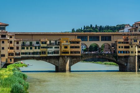 Florence, Italy - June 5, 2019 : The Ponte Vecchio (Old Bridge) is a medieval stone closed-spandrel segmental arch bridge over the Arno River, noted for having shops built along it. The present tenants are jewelers, art dealers and souvenir sellers.の写真素材