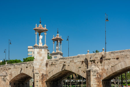 Pont del Mar stone bridge with the Virgin dels Desemparats monument standing above Turia Gardens' water channel under a clear blue skyの写真素材