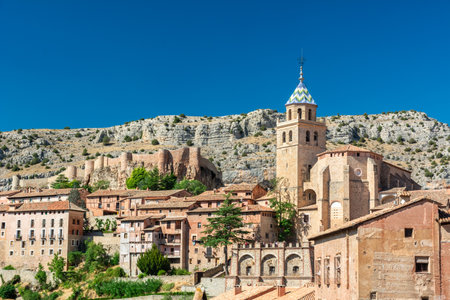 A sweeping view of Albarracin's cathedral tower, stone arches and hilltop fortress walls against a clear blue sky.の写真素材