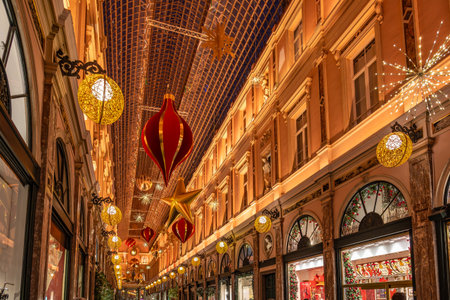 Brussels, Belgium - Nov 30, 2025: Christmas ornaments and golden lights hanging under the glass roof of the Galeries Royales Saint Hubert.のeditorial素材