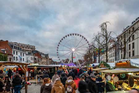 Brussels, Belgium - Nov 30, 2025: Crowds at the Winter Wonders Christmas market with the illuminated Ferris wheel rising above the festive wooden stalls.のeditorial素材