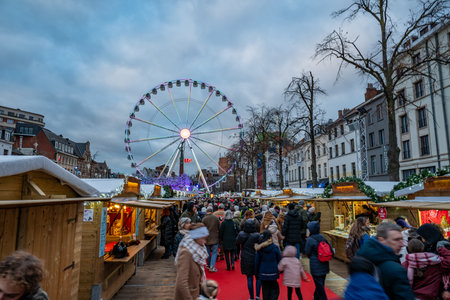 Brussels, Belgium - Nov 30, 2025: Crowds walking through the Winter Wonders Christmas market, with the illuminated Ferris wheel rising above festive wooden stalls.のeditorial素材