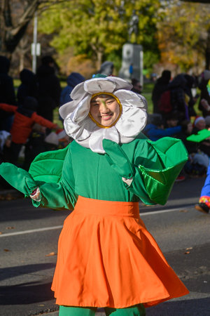 TORONTO, ONTARIO, CANADA - NOVEMBER 23, 2025: A participant wearing a brightly coloured flower (daisy) costume, with a large white petal headpiece, smiles as they proceed along the route of The Original Santa Claus Parade in Downtown Toronto.のeditorial素材