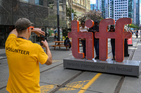 Toronto, ON, Canada - September 7, 2025: Volunteer taking a picture of three people smiling and posing with the large TIFF sign on a city street during the festivalのeditorial素材