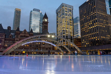 Toronto, ON, Canada - December 3, 2025: People enjoying winter ice skating at Nathan Phillips Square, with Toronto landmarks and modern buildings illuminated at duskのeditorial素材