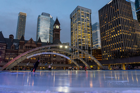 Toronto, ON, Canada - December 3, 2025: People enjoying winter ice skating at Nathan Phillips Square in Toronto, Canada, with modern city buildings illuminating the eveningのeditorial素材