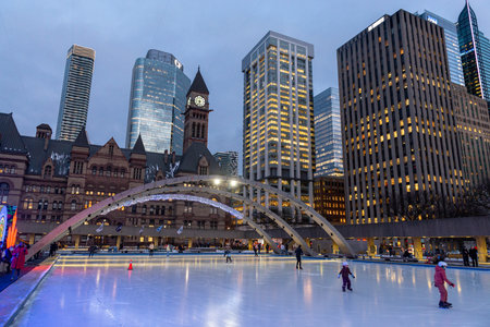 Toronto, ON, Canada - December 3, 2025: People ice skating in Nathan Phillips Square with Old City...