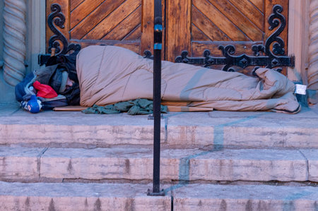 Toronto, ON, Canada - October, 15, 2025: Homeless person sleeping in a bag on cold stone steps by a doorway, illustrating urban poverty, marginalization and lack of shelterのeditorial素材