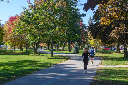 Toronto, ON, Canada - October 10, 2025: Two adults jogging along a tree-lined park pathway in Toronto, enjoying colorful autumn foliage and outdoor exerciseのeditorial素材