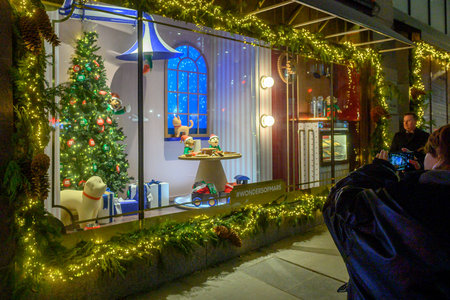 Toronto, On, Canada - December 23, 2025: Animated Christmas window display illuminating a city street, featuring decorative trees, elves, and gifts. People observing, recordingのeditorial素材