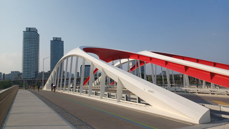 Toronto, ON, Canada - July 6, 2025: A modern arched bridge with yellow supporting beams spans a...