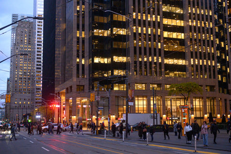 Toronto, ON, Canada - November 11, 2025: People cross a busy downtown street; the warm light spills...
