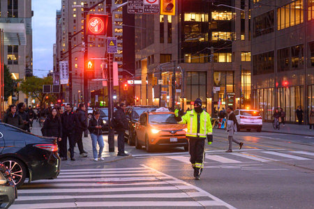 Toronto, ON, Canada - November 11, 2025: People walk at a crosswalk; A construction worker is...