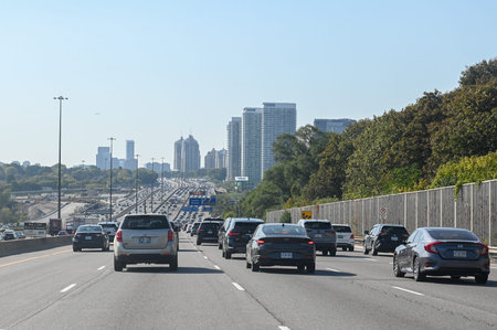 Toronto, ON, Canada - August 10, 2025: Cars drive on a busy highway with a city skyline visible in...