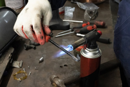 A crafstman holding a small blowtorch and working on a metal design project by burning the metal and...
