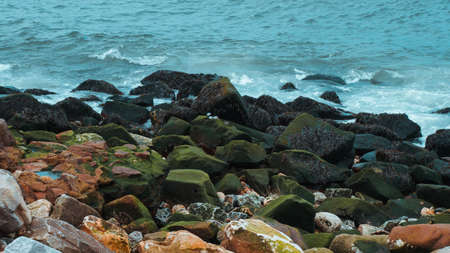 Photo of stones on the shore of the blue sea with waves.の写真素材