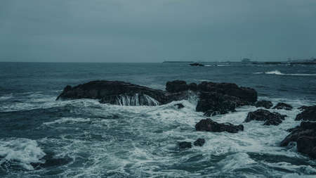 Photo of stones on the shore of the blue raging sea in a storm with waves.の写真素材