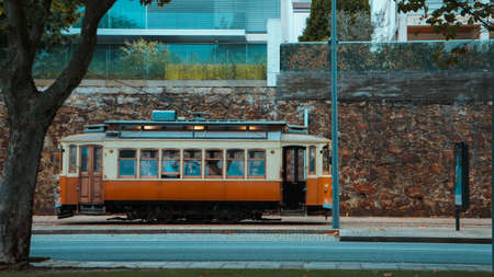 Photo of a yellow and orange tram in the city near the stone wall.の写真素材