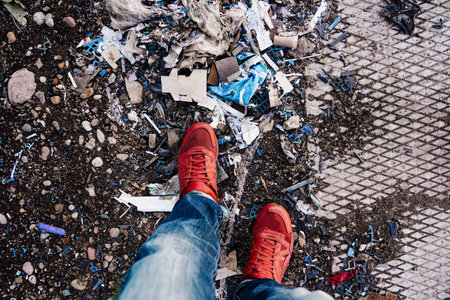 A man in red sneakers and blue jeans walks through a garbage dump.