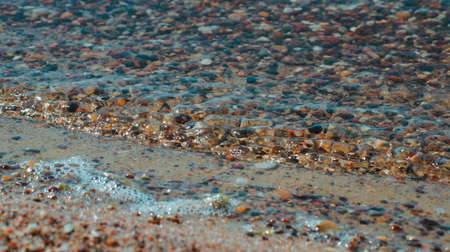 Close-up photo of stones on the shore of the blue sea with waves.の写真素材