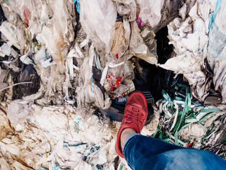 A man in red sneakers and blue jeans walks through a garbage dump.の写真素材