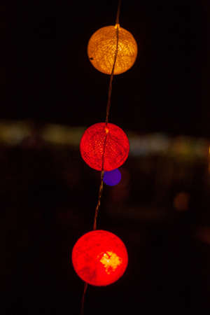 Close up vertical photo of three orange, yellow and red glowing round garlands on the street.の写真素材
