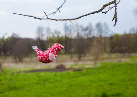 Photo of a red bird made of fabric made by hand hanging on a tree branch on the street.