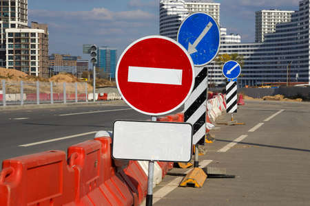 Photo of a round blue road sign with a white arrow, black and white rectangular sign and red and white round stop sign on the street in the city.の写真素材