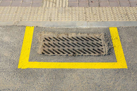 Photo of a drain for water fenced with a yellow drawn stripe on gray asphalt on the road in the city.の写真素材