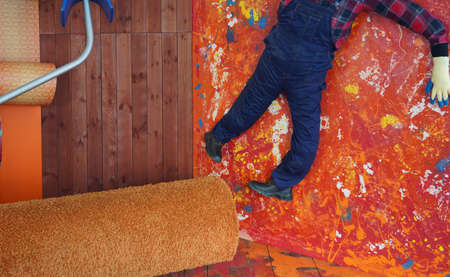 Photo of a man on a colored wall in paint next to a paint roller.
