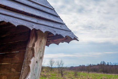 Photo of a wooden roof of a house in a village on the street against a background of sky and grass.