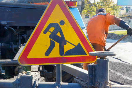 Photo of a red-yellow triangular road sign on the background of road works.
