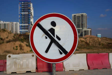 Photo of a round white-red road sign with a crossed out man on the background of a construction of...
