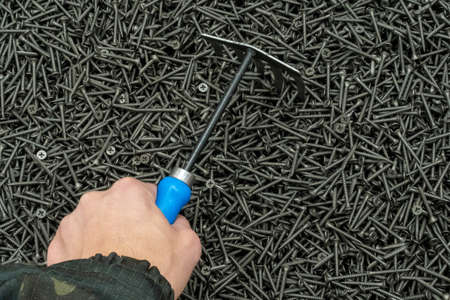 Photo of steel screws as a background and a man's hand with a rake. Hardware store.