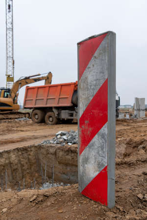 Vertical photo of a red and white sign at a construction site with a truck and an excavator in the background.の写真素材
