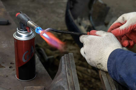 Photo of a gas burner and metal melting. Male hands in work gloves in the garage.の写真素材