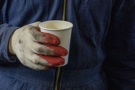 Photo of a white paper cup of coffee in the hands in gloves of a male worker.の写真素材