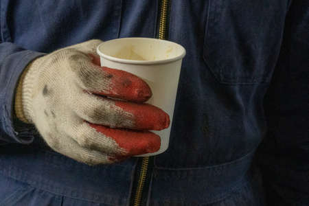 Photo of a white paper cup of coffee in the hands in gloves of a male worker.の写真素材