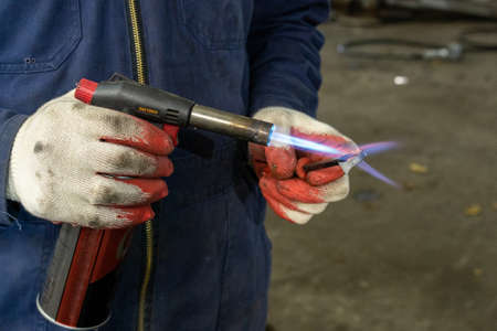 Photo of a gas burner and metal melting. Male hands in work gloves in the garage. Gas torchの写真素材