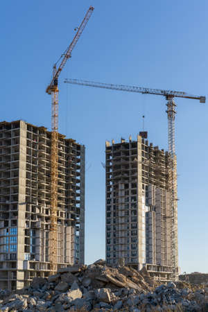 Vertical photo of the construction site and building of high buildings and cranes against blue clear sky in the city. Constructional concept.の写真素材