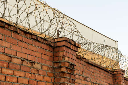 Photo of a red brick wall with barbed wire. Fencing and fence.の写真素材