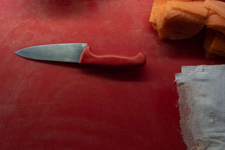 knife with a red handle on a cutting board with fish.
